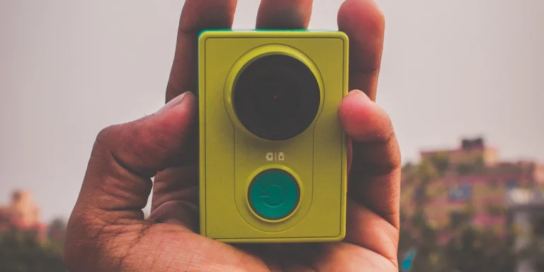07 best camera for filmmaking on a budget: Action Camera 20 Hand holding a compact yellow camera with green details against a blurred background.