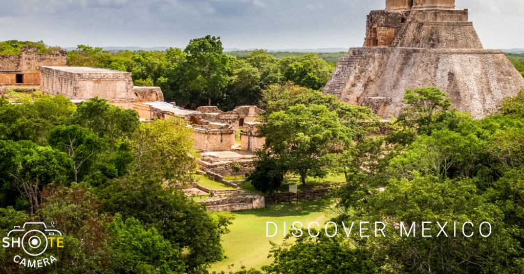 Top Travel Destinations for Photography Enthusiasts 7 A panoramic view of a large ancient pyramid in the midst of a lush green forest under a partly cloudy sky. The pyramid, which appears to be from the Mayan civilization, is made of stone and has a stairway leading up to the top. In the foreground, there are smaller ruins and trees scattered around the landscape. The image has text that reads ‘DISCOVER MEXICO’ in bold letters at the top right corner and a watermark at the bottom left corner that says ‘SHOTECAMERA’.