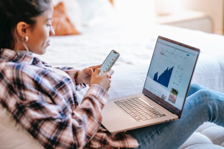 Application maintenance and support services: A critical investment for businesses 1 Person analyzing data on laptop while holding smartphone, depicting active business management. #Application maintenance